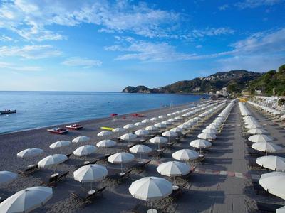 Beach with many white umbrellas and calm sea under blue sky.
