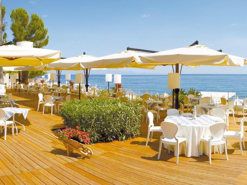 A terrace with tables, chairs, and umbrellas overlooking the sea under a clear sky.