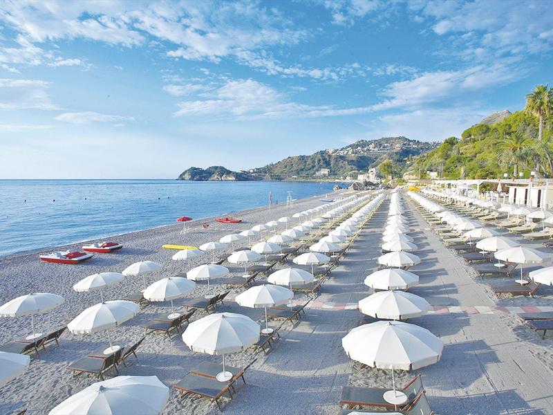 Row of white umbrellas and sun loungers on the beach overlooking the sea and mountains.