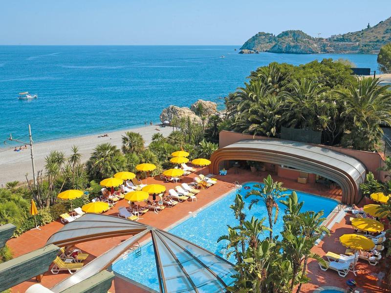 Hotel pool with yellow umbrellas next to a beach and clear blue sea.