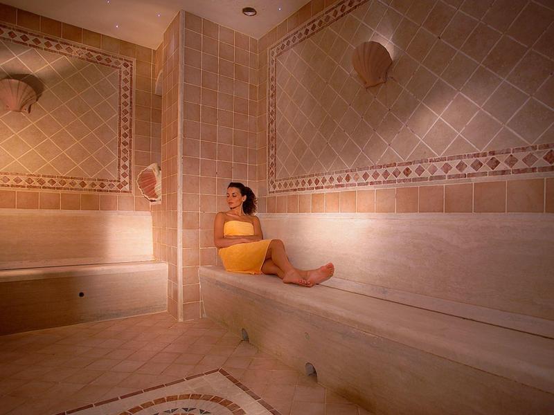 Woman relaxes in a warm-lit Turkish steam room with marble interior.