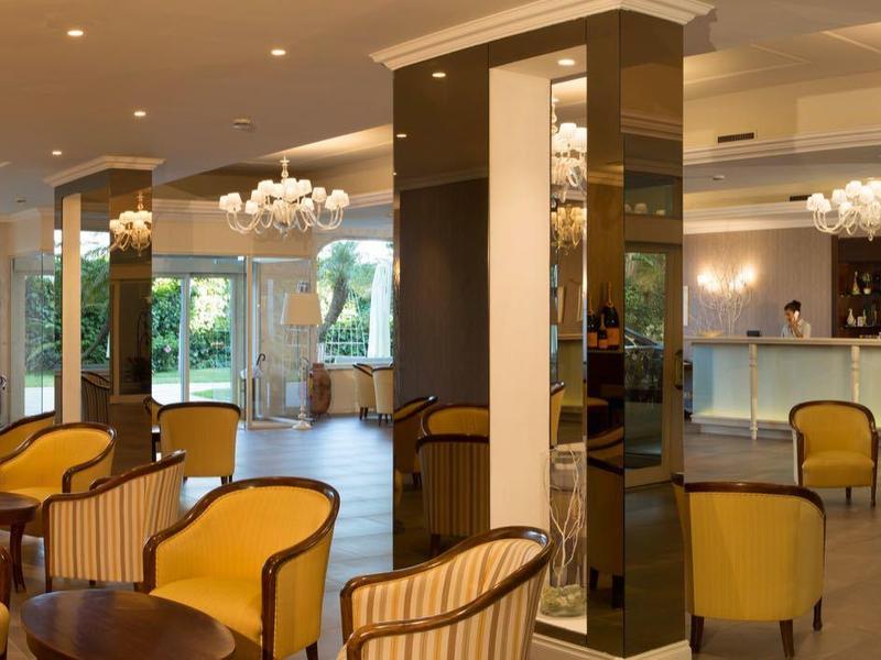 Elegant hotel lobby with yellow armchairs, wooden furniture, and large windows overlooking greenery.