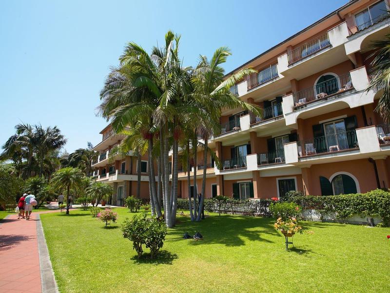 Hotel building with balconies, tropical palm trees, and a well-maintained green lawn.