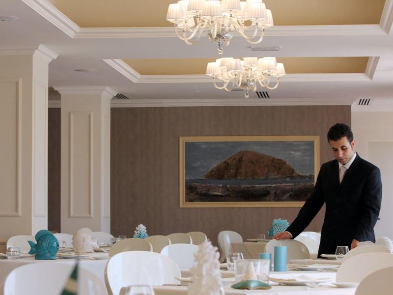 Elegant dining room with stylishly set tables and a staff member in formal attire.