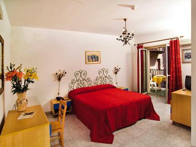 Hotelzimmer mit rotem Doppelbett, Holzmöbeln und einem Balkon mit Sitzgelegenheit.