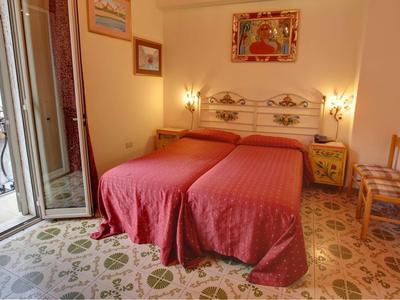 Pokój z dwoma pojedynczymi łóżkami, czerwonymi narzutami i balkonem z widokiem na zewnątrz.