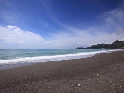 Plaża z ciemnym piaskiem i spokojnym morzem pod niebieskim niebem z kilkoma chmurami