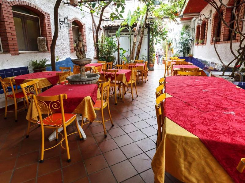 Przytulny dziedziniec z żółtymi krzesłami i stołami przykrytymi czerwonymi i żółtymi obrusami.