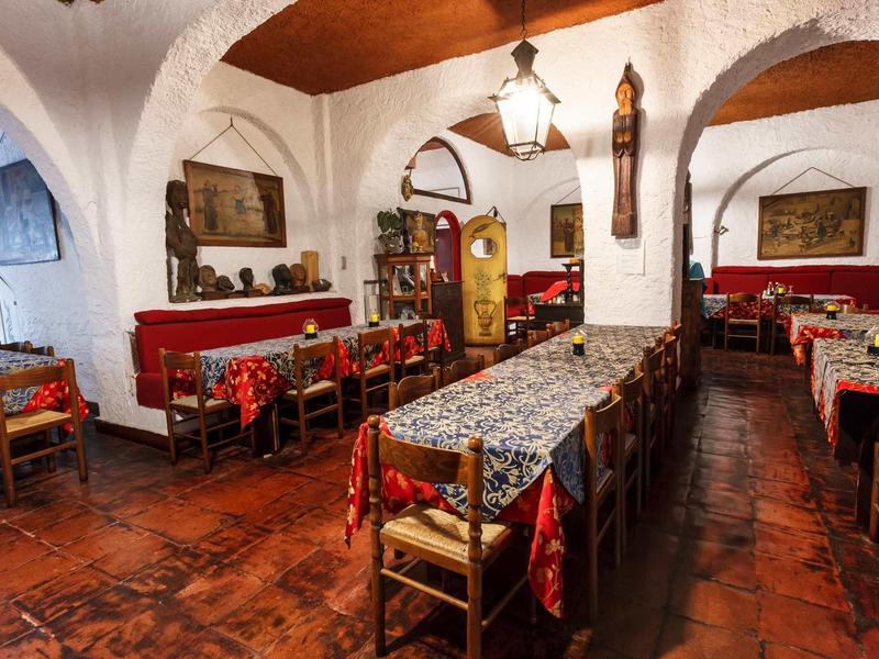 Rustykalna restauracja z długimi drewnianymi stołami, krzesłami i przytulną atmosferą.