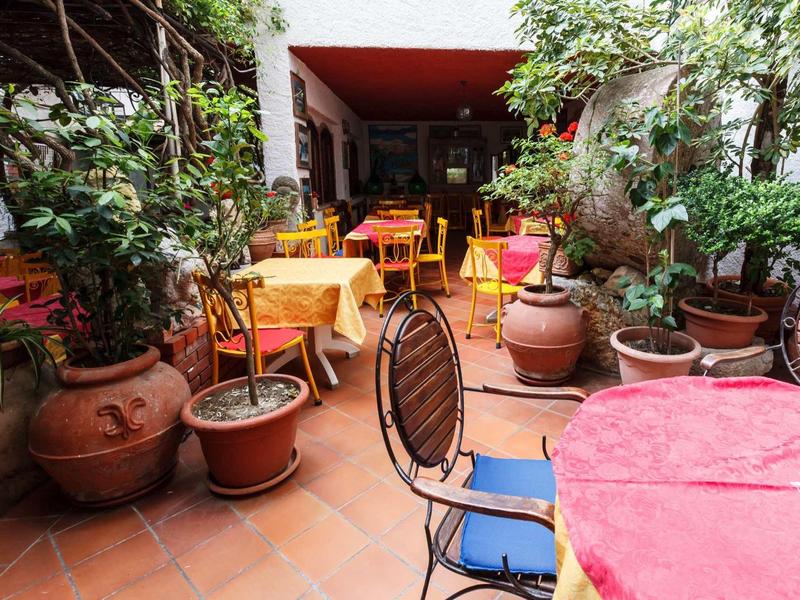 Przytulne podwórze z stołami, krzesłami i doniczkami pod czerwonym dachem.