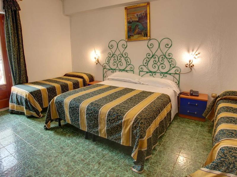 Pokój trzyosobowy z trzema łóżkami z pasiastymi narzutami i zieloną podłogą z płytek.