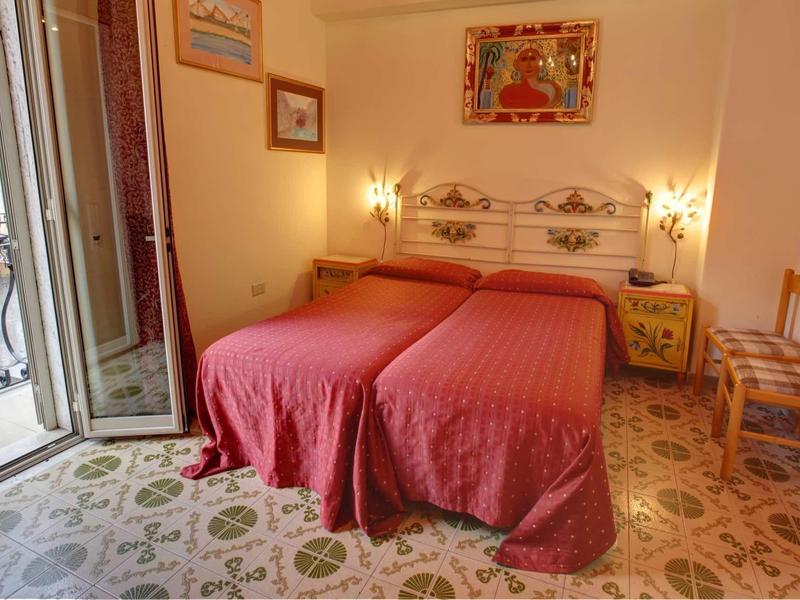 Pokój z dwoma pojedynczymi łóżkami, czerwonymi narzutami i balkonem z widokiem na zewnątrz.