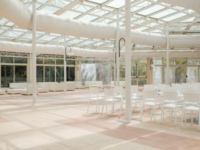 Duże, jasne pomieszczenie z wieloma białymi krzesłami i szklanym dachem, idealne na wydarzenia.