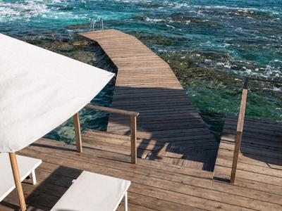 Holzsteg führt über Felsen ins klare, blau-grüne Meer an einem sonnigen Tag.