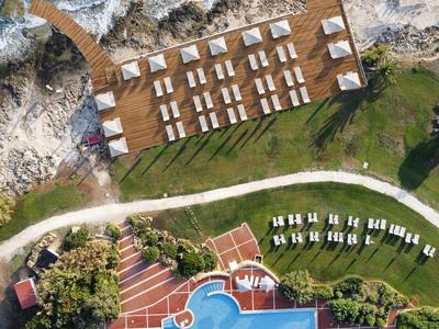 Vue aérienne d'un hôtel avec piscine, transats et une promenade côtière au bord de la mer