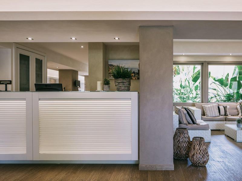 Modern gestalteter Empfangsbereich mit weißem Tresen, Holzboden und Sitzbereich mit Pflanzen am Fenster.