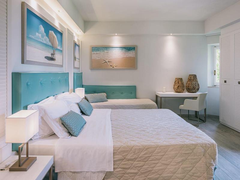 Modernes Schlafzimmer mit zwei Betten, türkisfarbenen Kopfteilen, weißen Wänden und dekorativen Bildern.