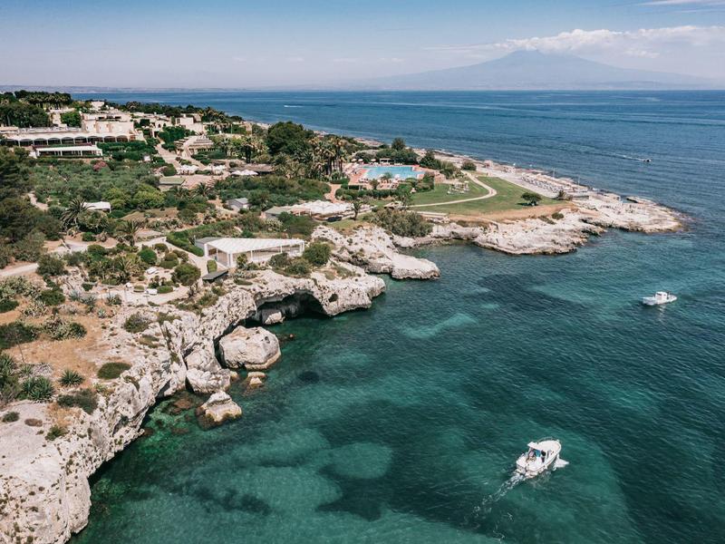 Küstenlandschaft mit klarem blauem Wasser, felsiger Uferlinie und einem kleinen Boot auf dem Meer.