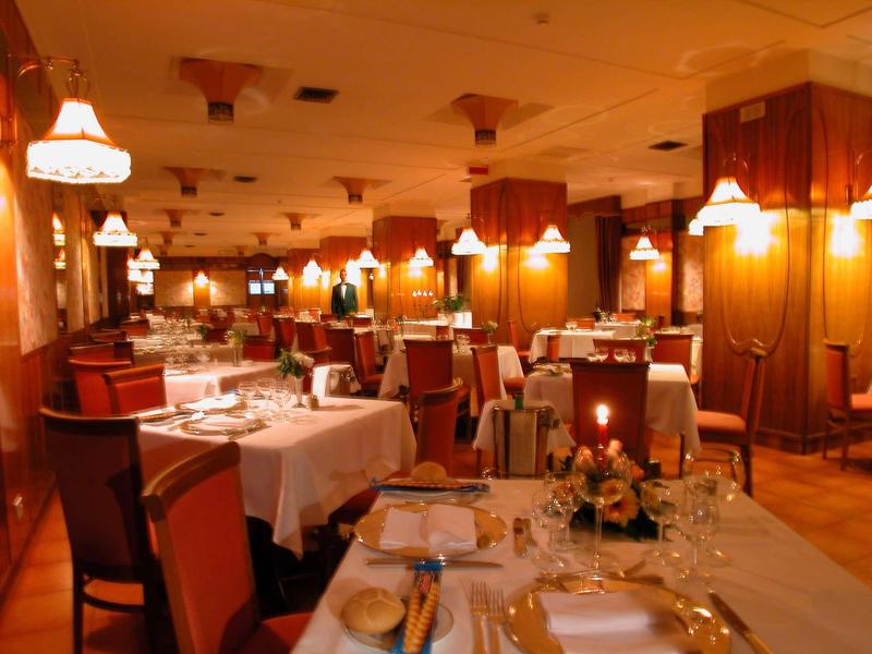 Elegancka sala restauracyjna hotelu z nakrytymi stołami i ciepłym oświetleniem.