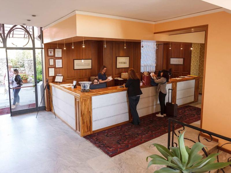 Recepcja hotelowa z gośćmi i personelem, przyjazna atmosfera, drewniany lada i dywan