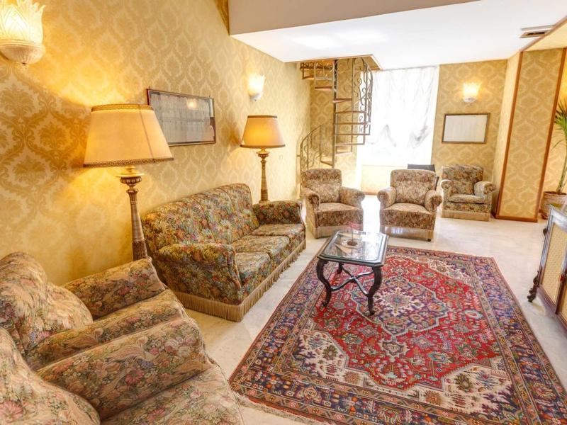 Przytulny salon z wzorzystymi fotelami, sofą, dywanem i ciepłym oświetleniem.