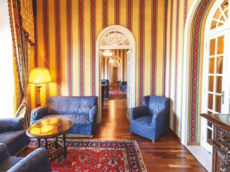 Elegancki salon z klasycznym umeblowaniem, niebieskimi sofami i czerwonym dywanem w wzory.