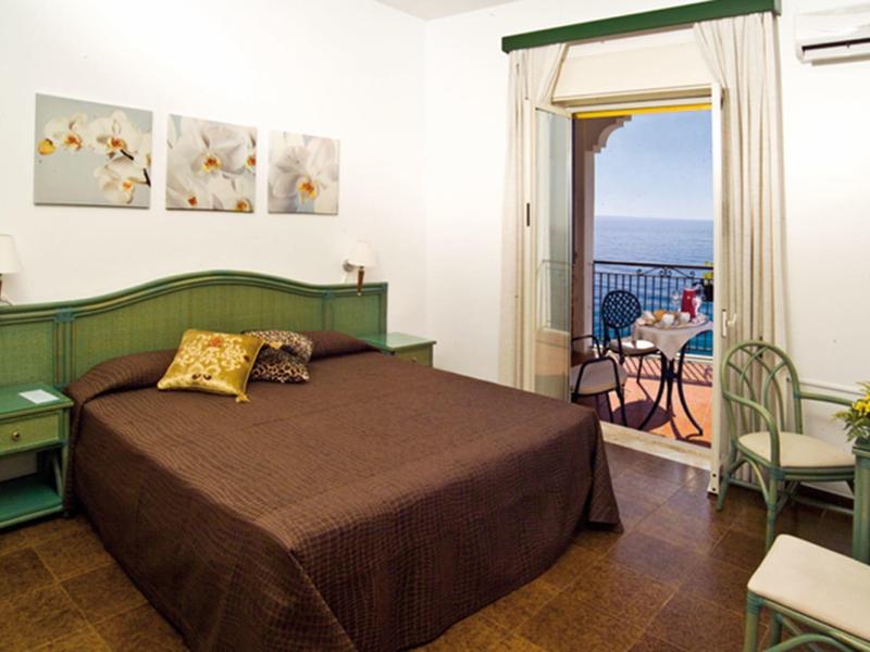 Sypialnia z podwójnym łóżkiem, zielonym umeblowaniem i balkonem z widokiem na morze.