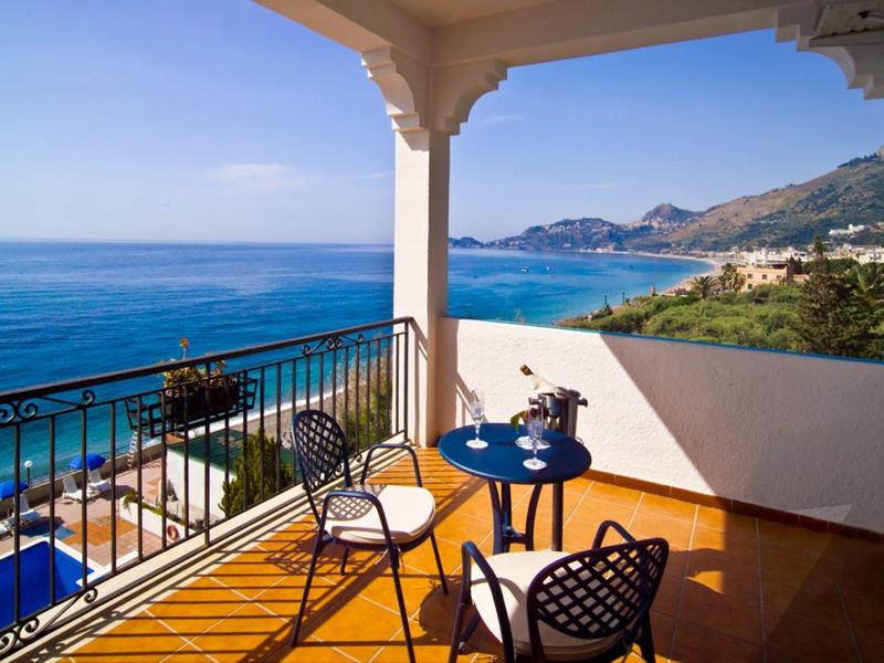 Balkon z krzesłami i stołem z widokiem na morze i góry pod czystym niebem.