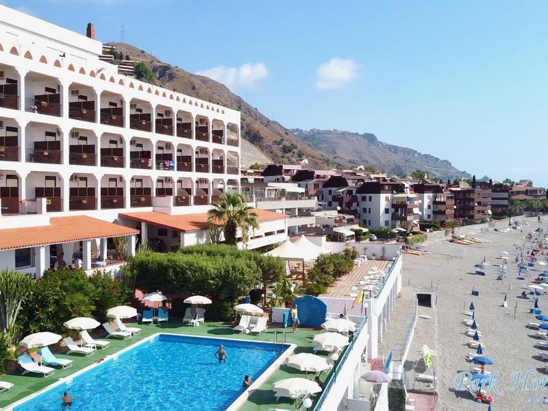 Kompleks hotelowy z basenem i leżakami na szerokiej piaszczystej plaży obok gór.