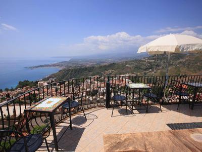 Balkon mit Tischen und Stühlen bietet Blick auf Küstenstadt und das Meer bei klarem Himmel.