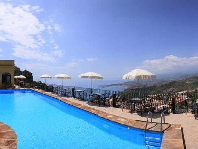 Hotelzwembad met parasols en ligstoelen met uitzicht op bergen en heldere lucht.