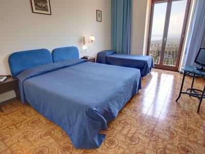 Hotelkamer met twee bedden, blauwe bedspreien en uitzicht op balkondeur met gordijnen.