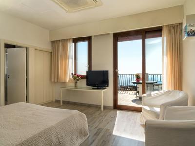 Helles Hotelzimmer mit Balkon, Meerblick, zwei Sesseln und Flachbildfernseher.