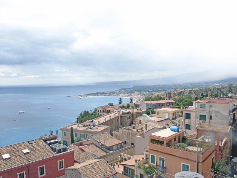 View over rooftops of a coastal town with sea and cloudy sky in the background.