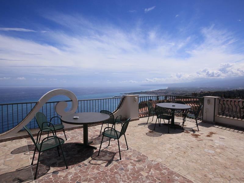 Open terrace with chairs and tables overlooking the sea under a blue sky.