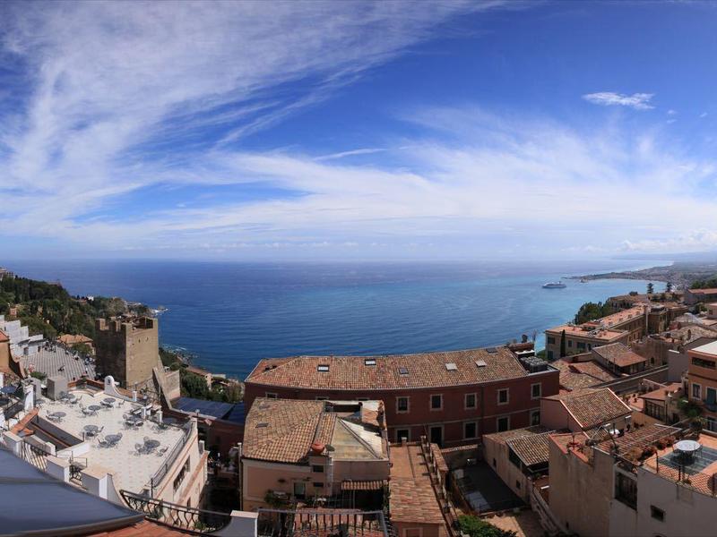 Panoramic view of a coastal town with terracotta roofs and blue sky.