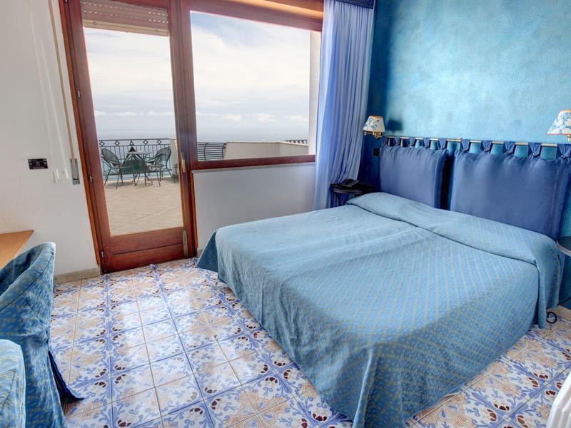 Bright hotel room with double bed and balcony overlooking the sea.