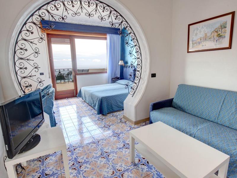 Bright hotel room with blue sofa, bed, balcony, and decorative arch.