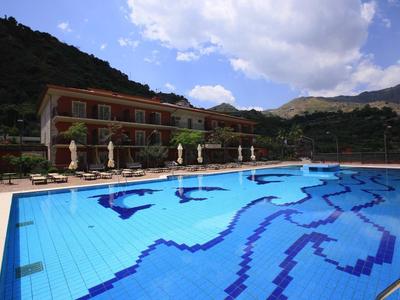 Großer blauer Swimmingpool mit Delfindekor vor mehrstöckigem Hotel und bewölktem Himmel.