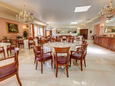 Großer Speisesaal mit runden Holztischen, Stühlen und Kronleuchtern an der Decke.