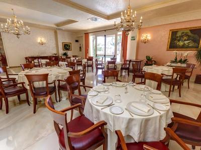 Elegantes Restaurant mit runden Tischen, weißen Tischdecken, roten Stühlen und Kronleuchtern.