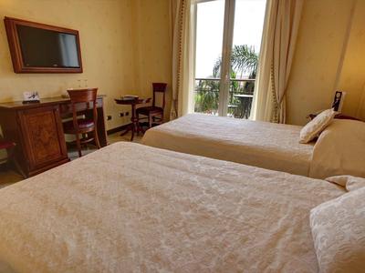 Hell eingerichtetes Schlafzimmer mit zwei Einzelbetten, Schreibtisch, Stuhl und Balkon mit Blick.