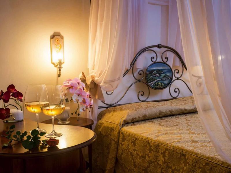 Gemütliches Schlafzimmer mit schmiedeeisernem Bett, goldenem Bettüberwurf und Blumen auf Nachttisch.