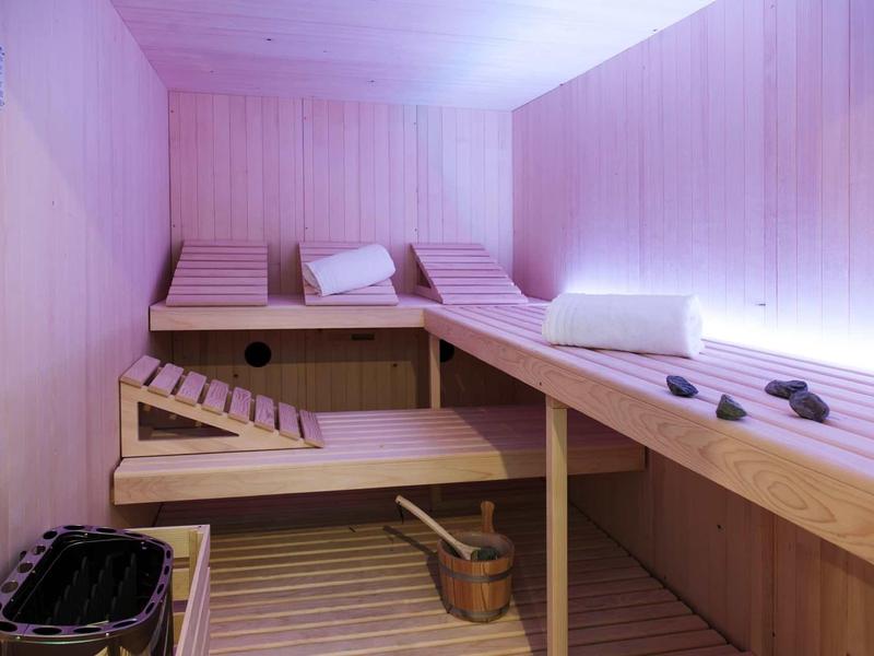 Moderne Holzsauna mit Liegen, Kopfkissen, Eimer, Schöpfkelle und Saunaofen mit Steinen.