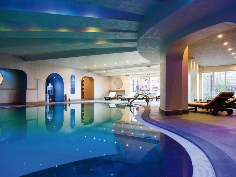 Moderner Innenpool mit blauen Fliesen, abgerundeten Säulen und gemütlichen Liegestühlen.