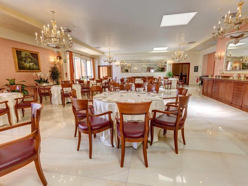 Großer Speisesaal mit runden Holztischen, Stühlen und Kronleuchtern an der Decke.