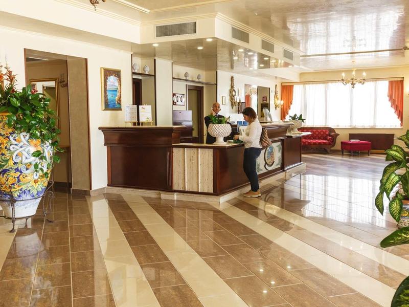 Große Hotellobby mit glänzendem Marmorboden, Holzempfangstresen und großen Pflanzen.