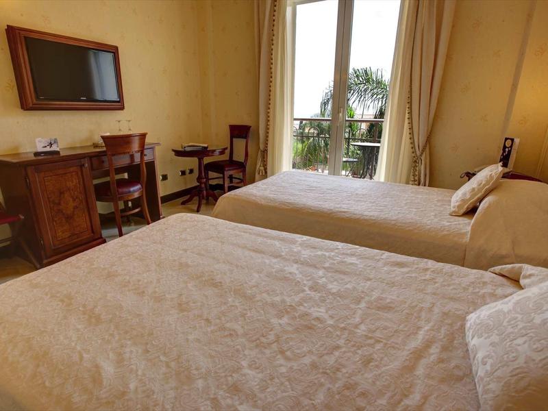 Hell eingerichtetes Schlafzimmer mit zwei Einzelbetten, Schreibtisch, Stuhl und Balkon mit Blick.