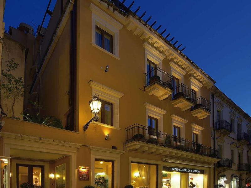 Illuminated hotel building with balconies on a narrow city street at night.