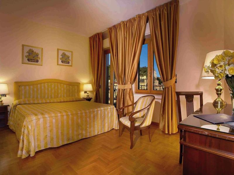 Cozy hotel room with double bed, chairs, and nighttime balcony view.